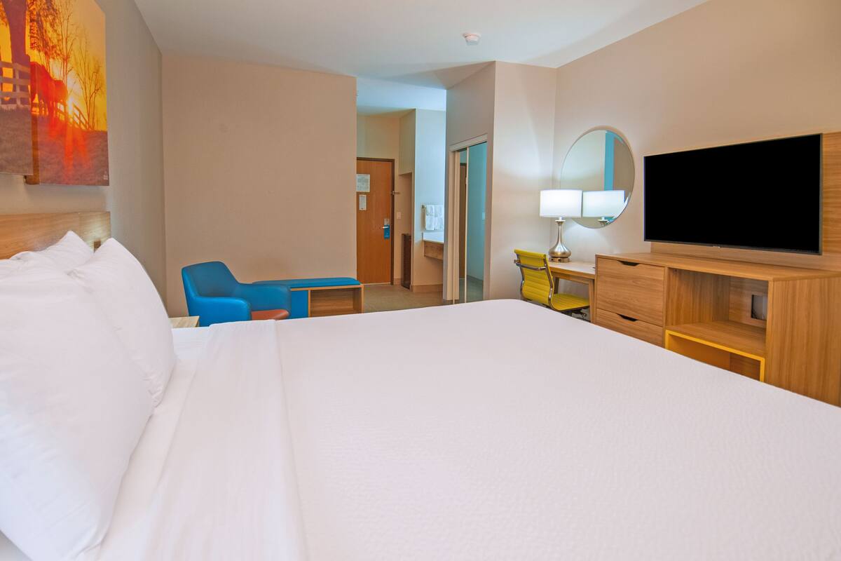Ein Hotelzimmer mit einem großen Bett, einem Schreibtisch mit Lampe, einem Fernseher und einem Sessel.