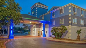 A hotel entrance with a covered driveway, a flag, and a building with a tower.