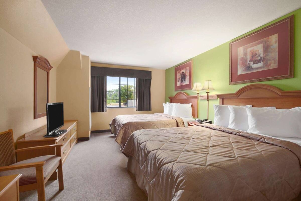 Ein Hotelzimmer mit zwei Betten, einem Fernseher, einem Schreibtisch und einem Fenster.