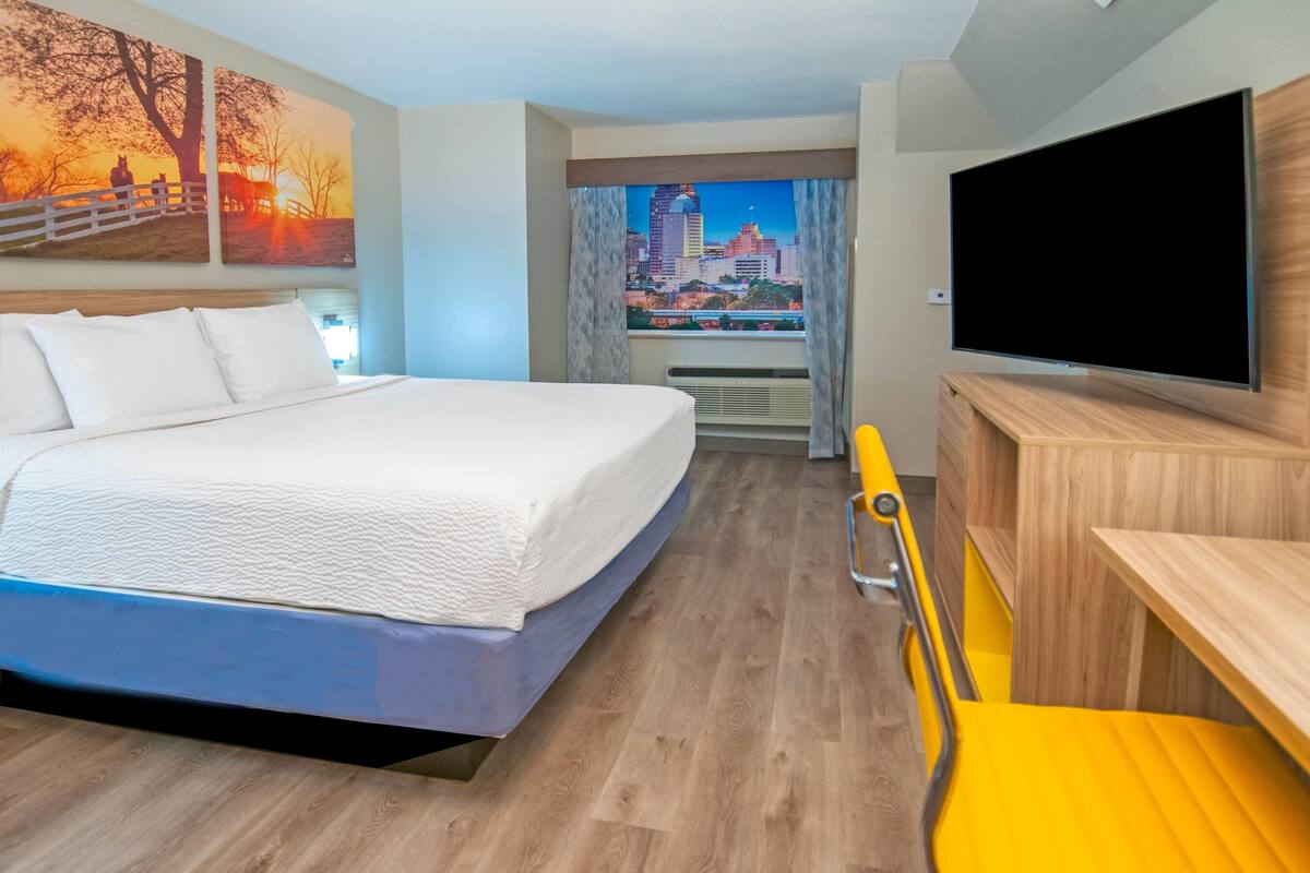Ein Hotelzimmer mit Bett, Fernseher, Schreibtisch und Fenster mit Blick auf die Stadt.