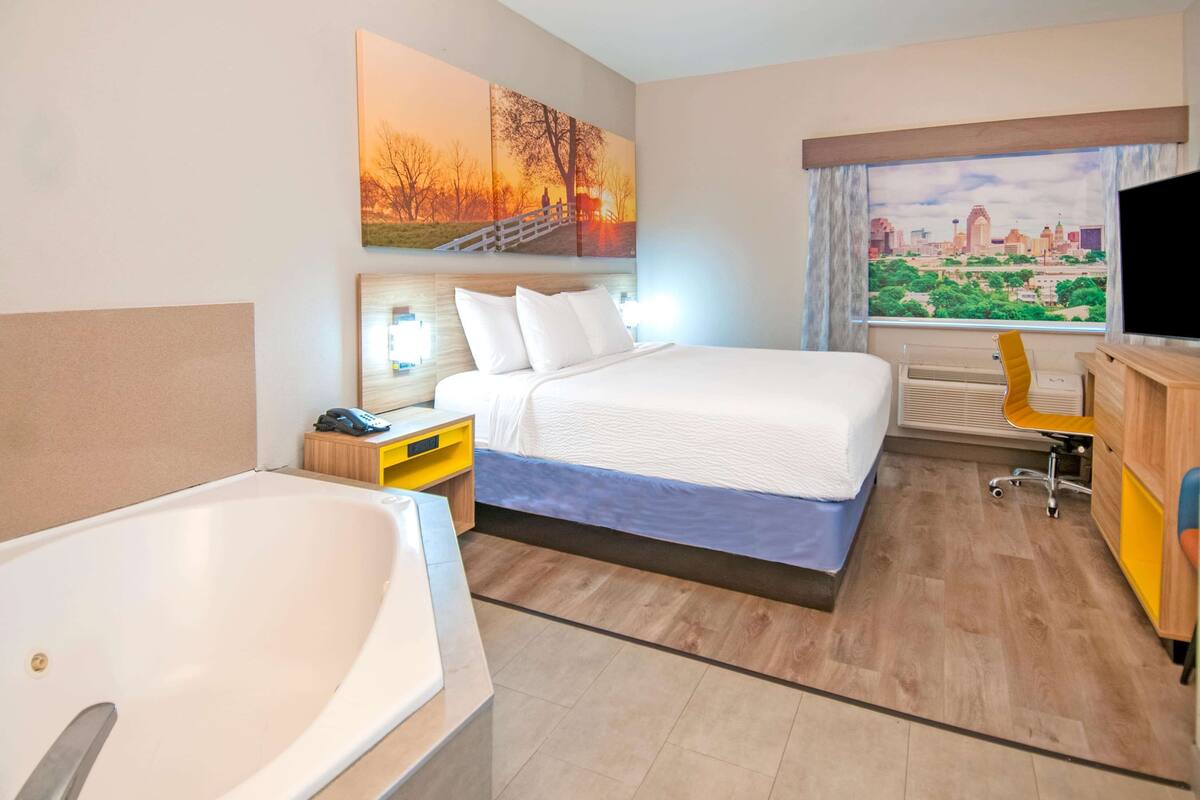 Ein Hotelzimmer mit einem großen Bett, einem separaten Schreibtischbereich, einer Badewanne und Blick auf die Stadt durch das Fenster.