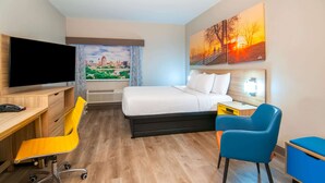 A hotel room with a bed, a desk with a chair, a television, and artwork on the walls.