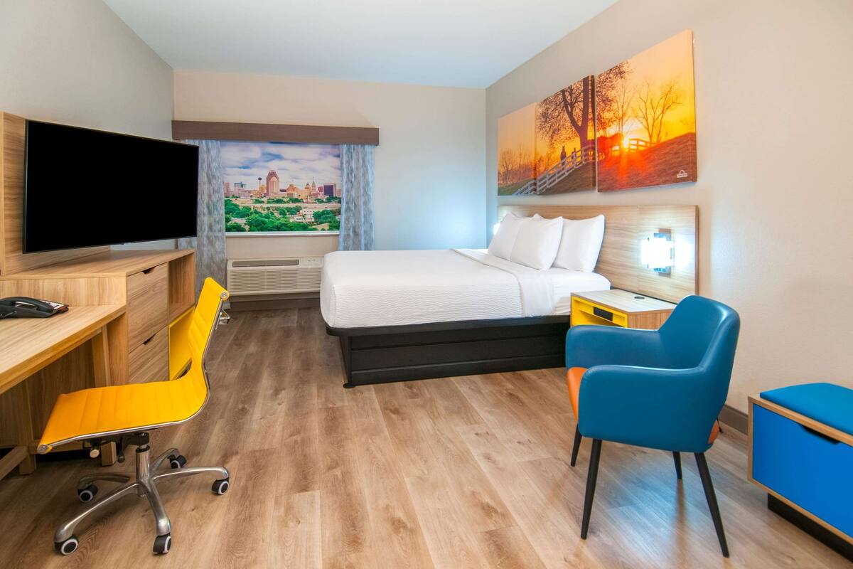 Ein Hotelzimmer mit Bett, Schreibtisch mit Stuhl, Fernseher und Bildern an den Wänden.