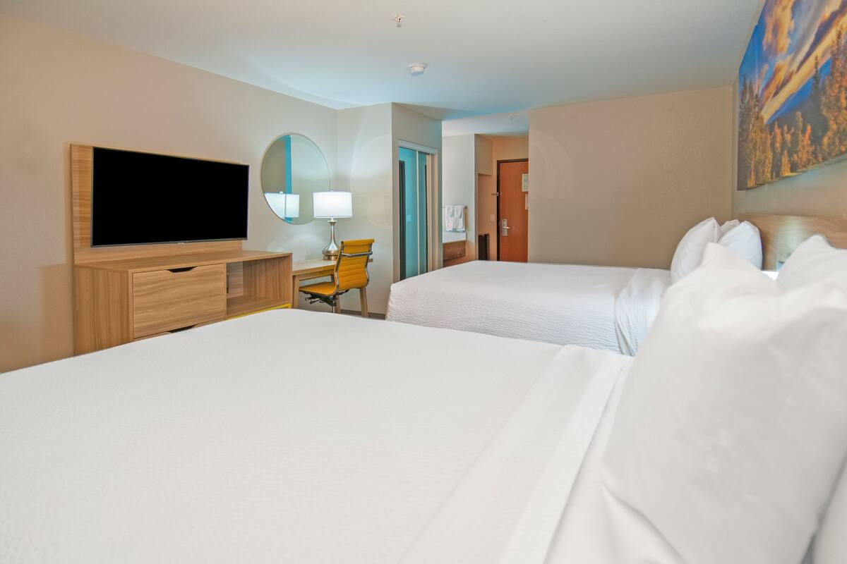 Ein Hotelzimmer mit zwei Betten, einem Fernseher, einem Schreibtisch mit Stuhl und einem Bild an der Wand.