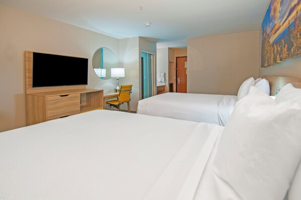A hotel room with two beds, a TV, a desk with a chair, and a painting on the wall.