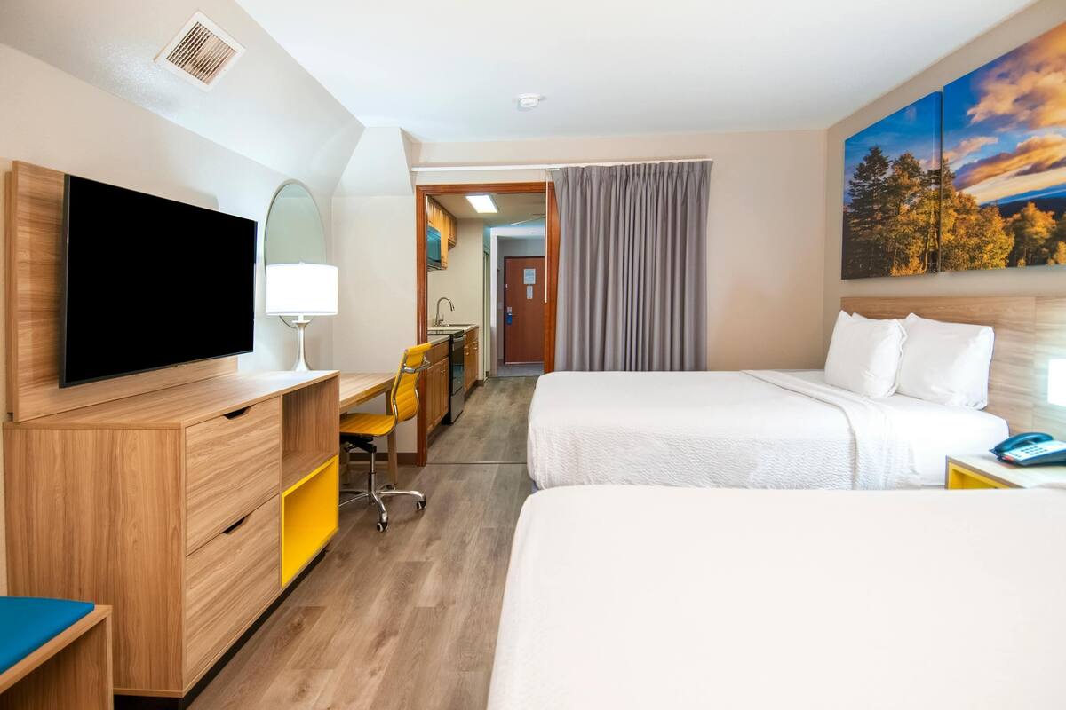 Ein Hotelzimmer mit Fernseher, Schreibtisch, Stuhl, zwei Betten und einem Gemälde.