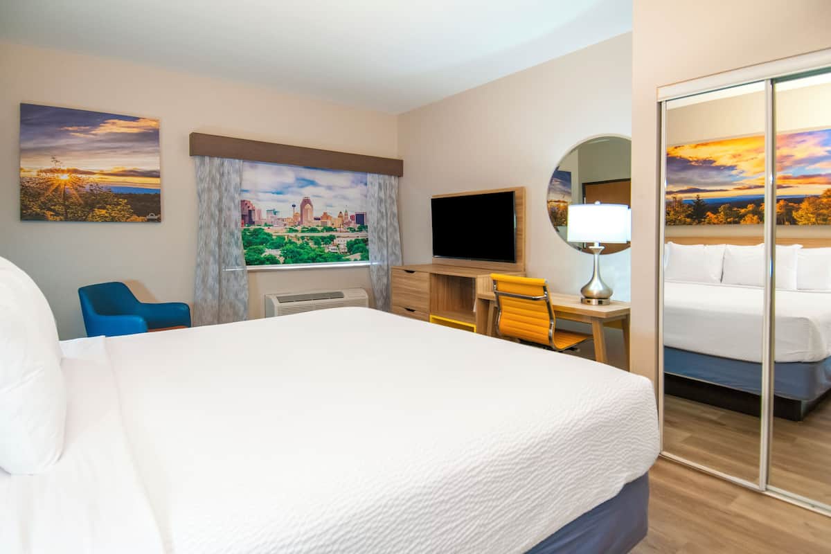 Ein Hotelzimmer mit einem großen Bett, einem Schreibtisch mit Stuhl, einem Flachbildfernseher, einem Fenster mit Vorhängen und einem Stadtbild.