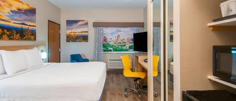 A hotel room with a bed, a desk with a chair, a television, and a cityscape view.