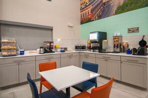 A modern kitchen with a white table and orange chairs, equipped with a coffee machine, toaster, and microwave. - Days Inn by Wyndham Suites San Antonio North/Stone Oak (San Antonio)