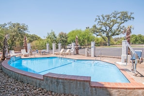 A swimming pool with a brick border, surrounded by lounge chairs and a stone fence. - Days Inn by Wyndham Suites San Antonio North/Stone Oak (San Antonio)