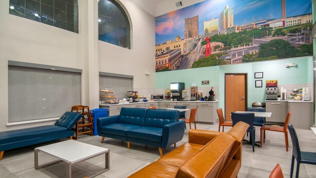 A modern hotel lobby with seating areas, a kitchen, and a mural of a cityscape.