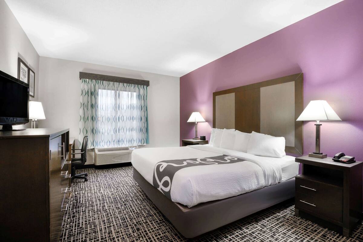 A hotel room with a large bed, two bedside lamps, a desk with a lamp, a chair, and a television.