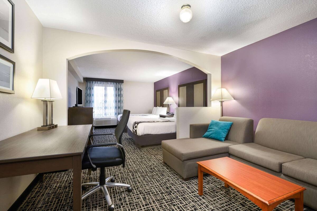 A hotel room with a bed, a sofa, a desk with a chair, and a TV.