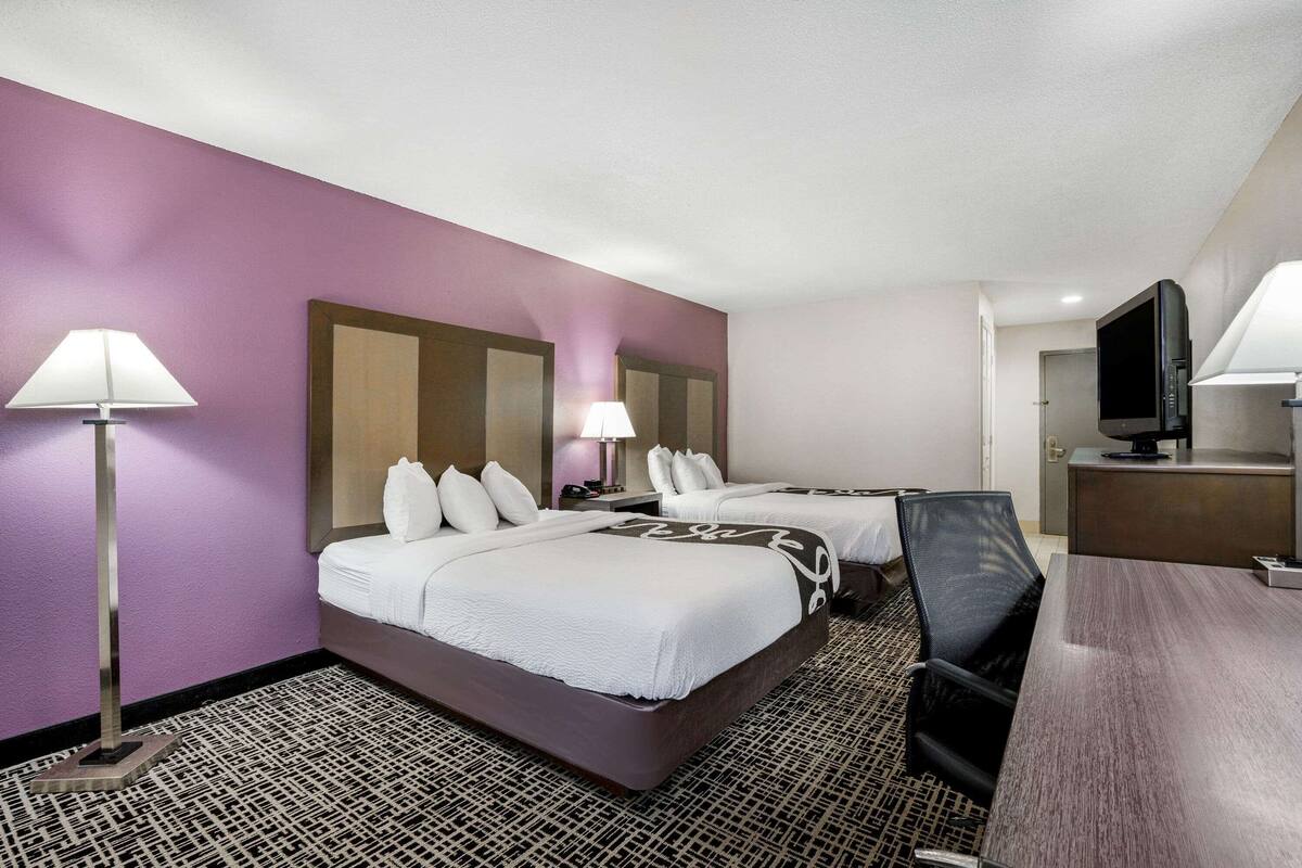 A hotel room with two beds, a desk, a TV, and a lamp.