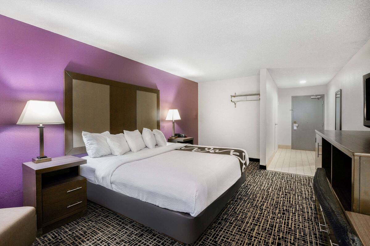 A hotel room with a large bed, two bedside tables with lamps, a TV, and a mirror.