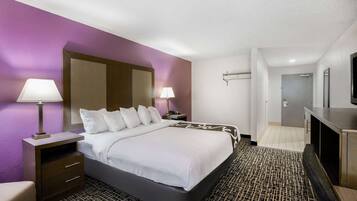 Quarto de hotel com uma cama grande, duas mesas de cabeceira com luminárias, uma TV e um espelho.
