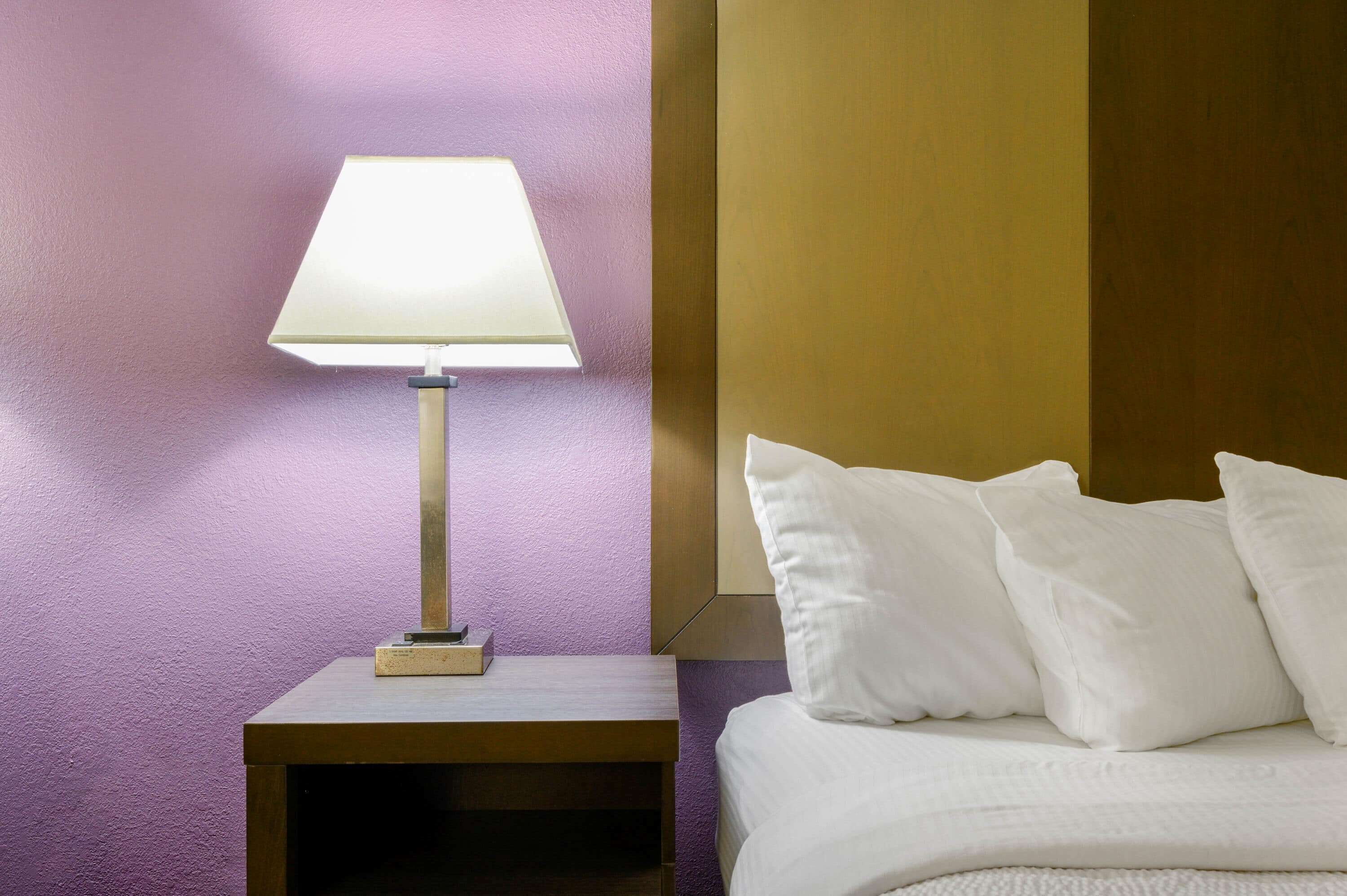 Una cama bien hecha con almohadas blancas y una mesita de noche con lámpara.