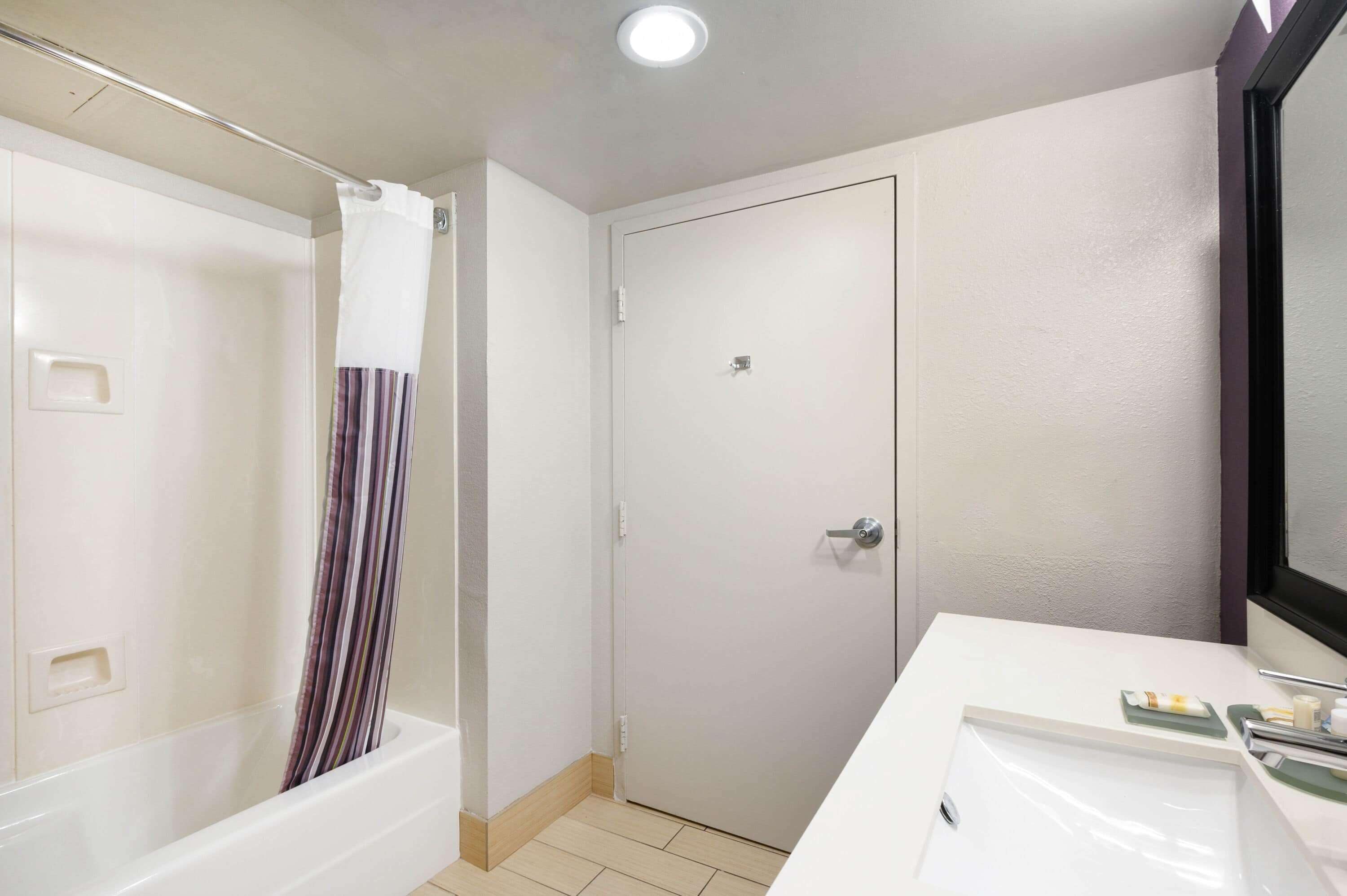 Un baño con bañera, cortina de ducha, puerta y lavamanos con artículos de aseo.