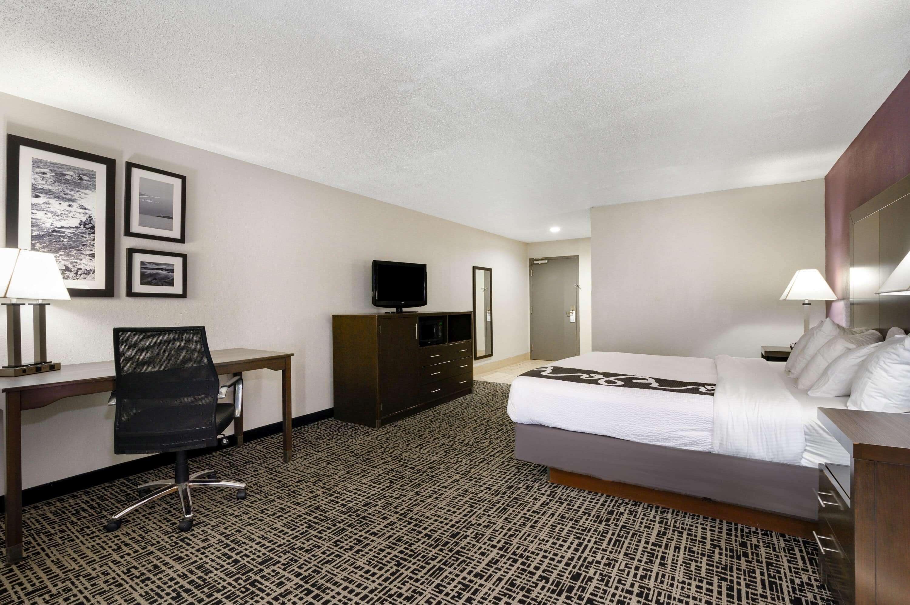 Een hotelkamer met een bed, bureau, stoel, televisie en een garderobekast.