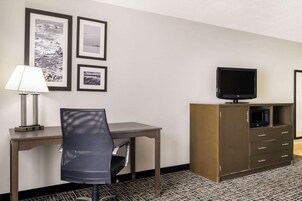 A hotel room with a desk, chair, TV, microwave, and framed pictures on the wall.