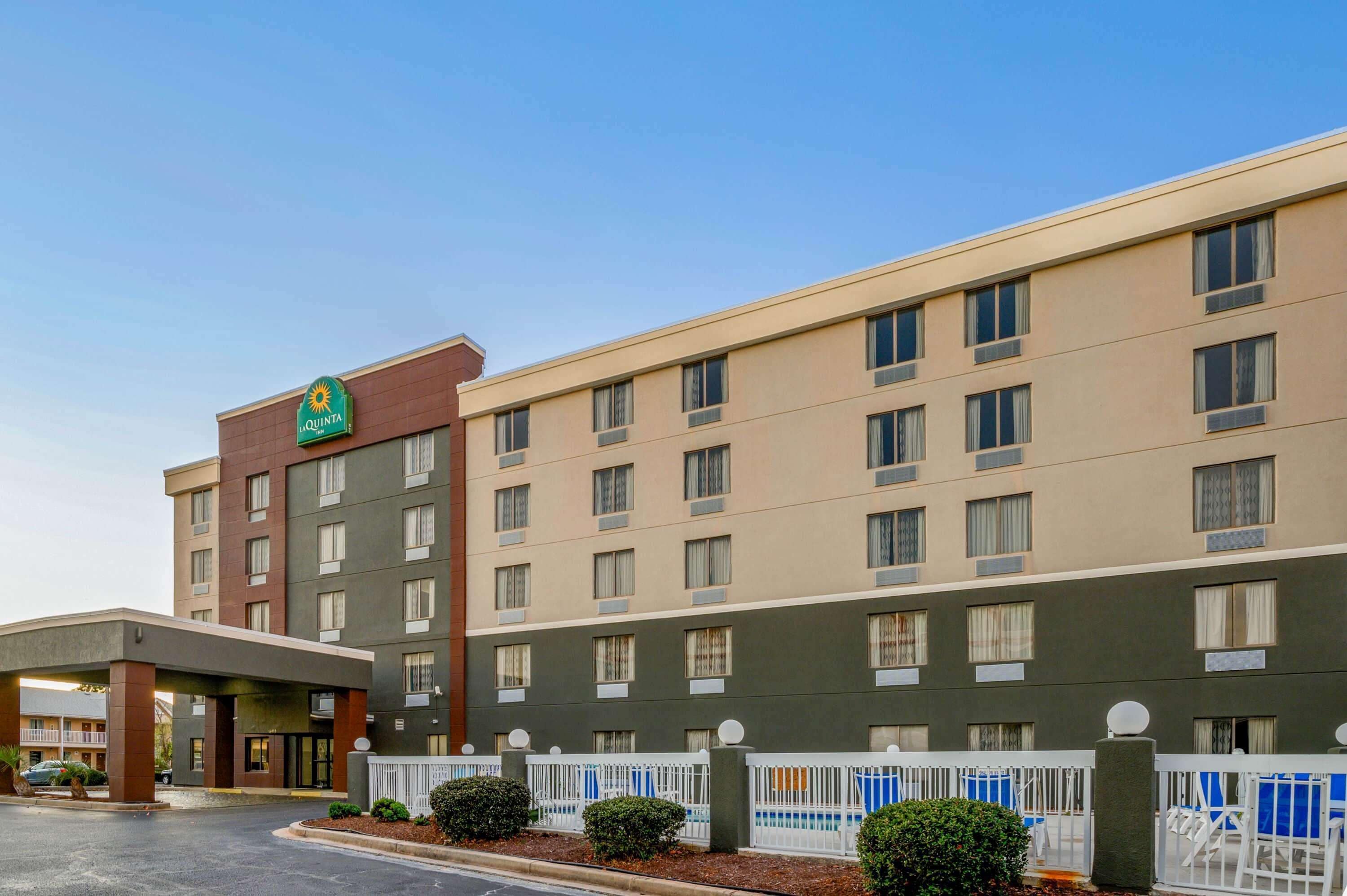 A multi-story hotel with a prominent 'QUINTA' sign, a covered entrance, and a fenced outdoor area with seating.