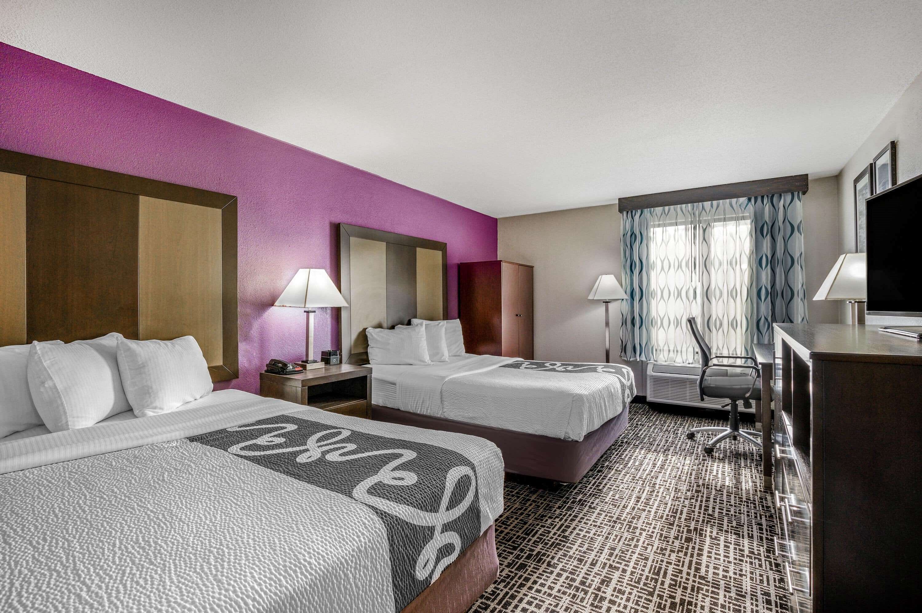 A hotel room with two beds, a desk, a chair, and a TV.