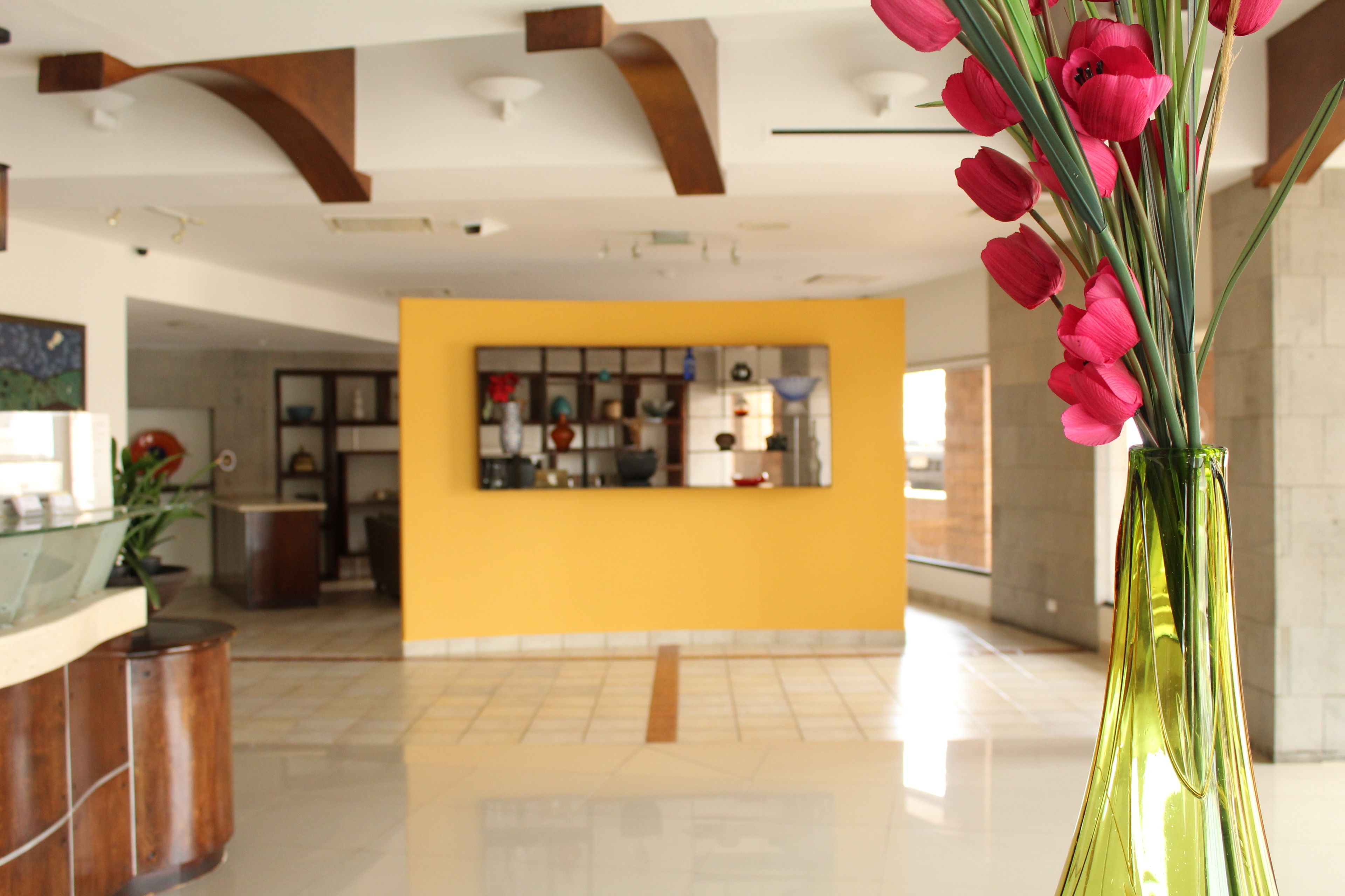 A lobby with a yellow wall, a reception desk, and a green vase with pink flowers.