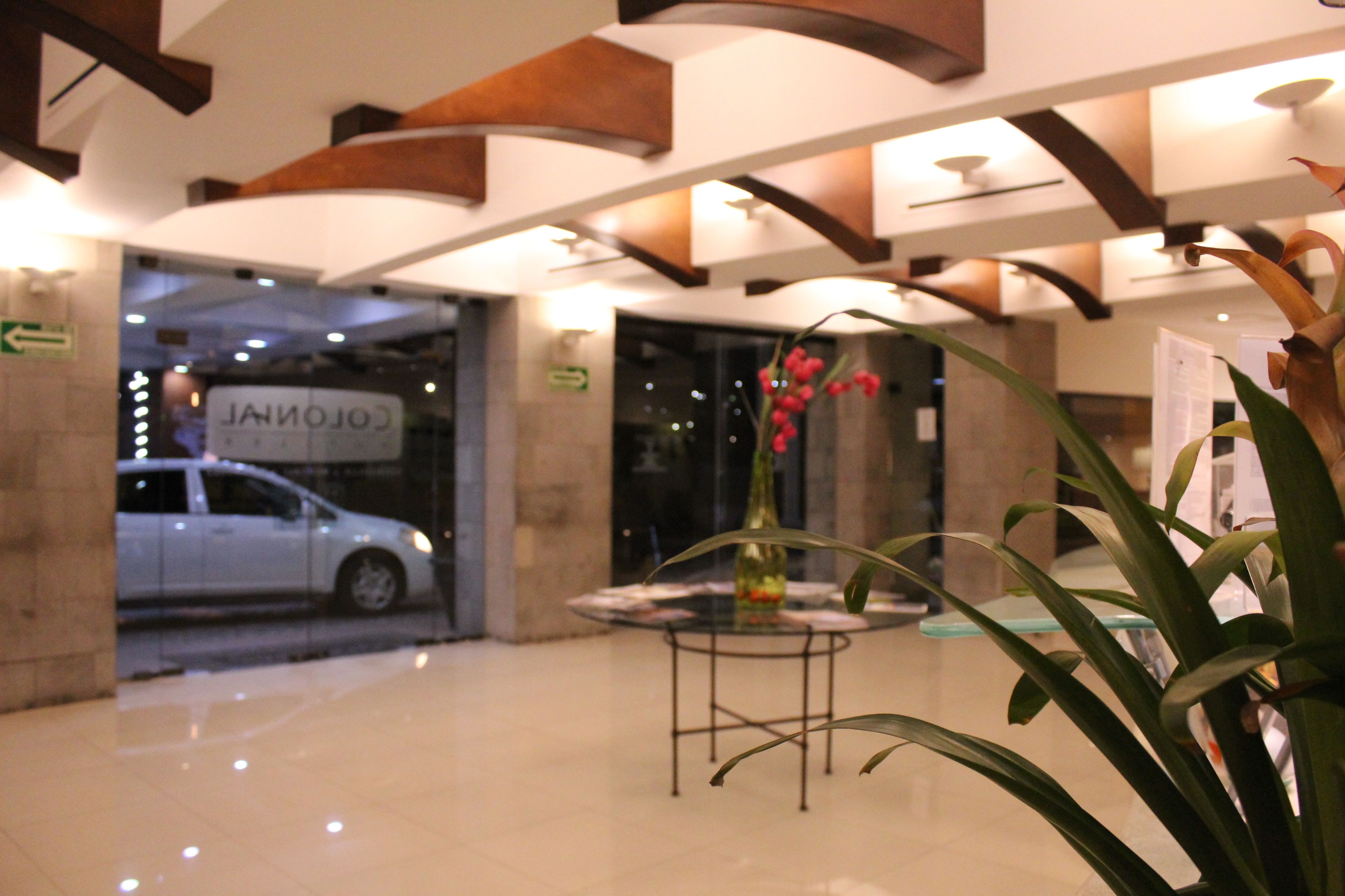 A lobby with a glass table, a plant, and a car parked outside.