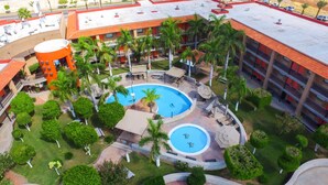 A hotel with two swimming pools, palm trees, and a red-roofed building.