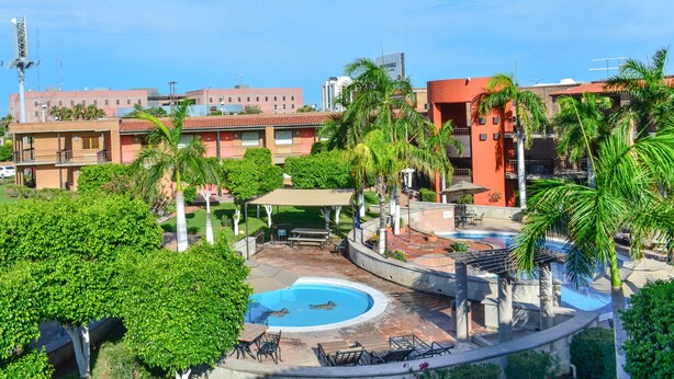 A resort with a swimming pool, outdoor seating, and palm trees.
