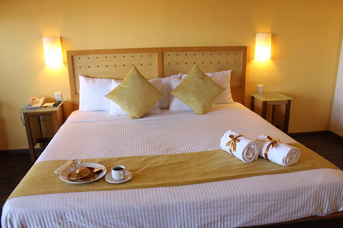 Ett hotellrum med en säng, två sängbord, en telefon, ett bricka med mat och en kopp samt handdukar.