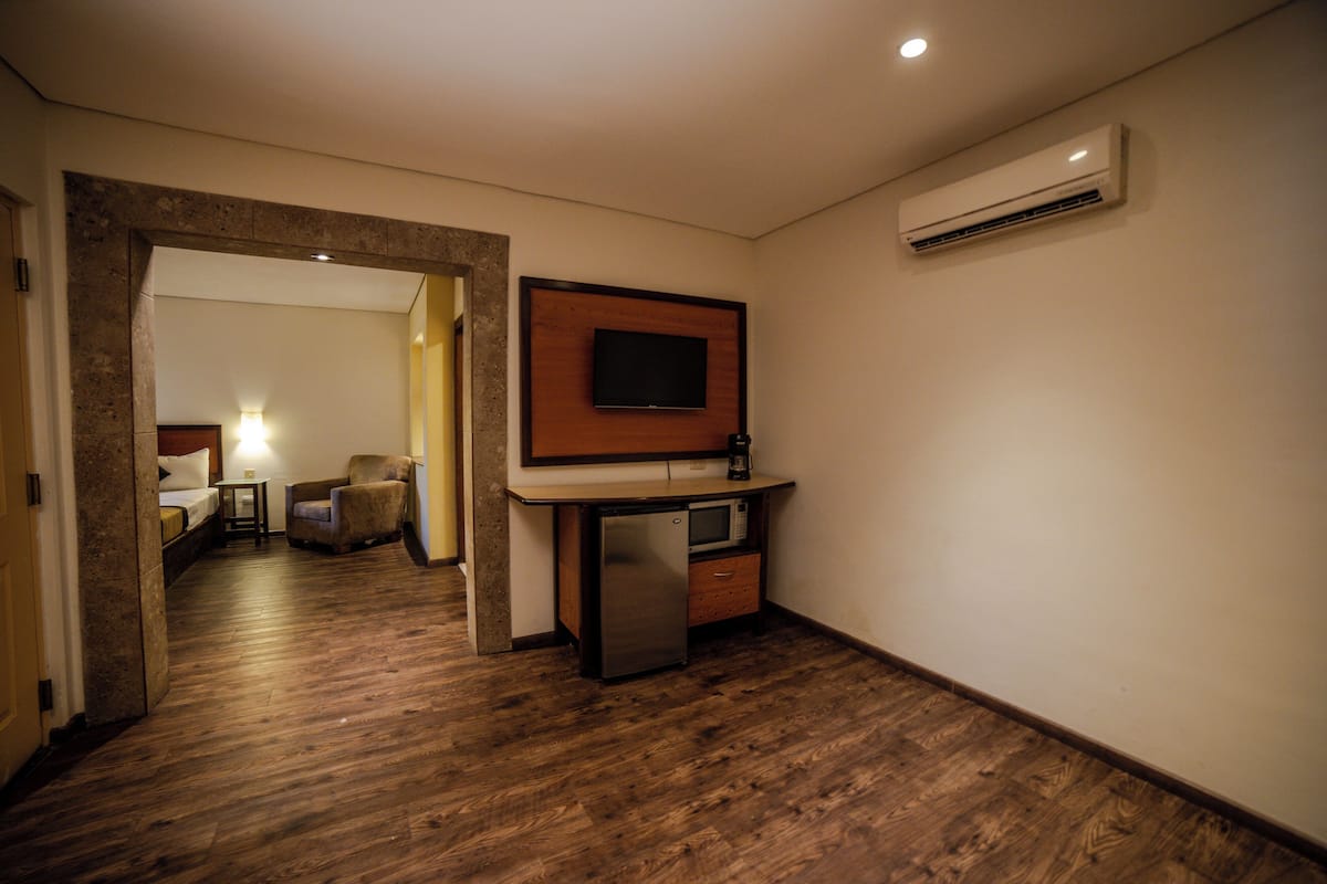 Ett kompakt hotellrum med ett litet kök, en platt-TV som är monterad på väggen och ett trägolv.