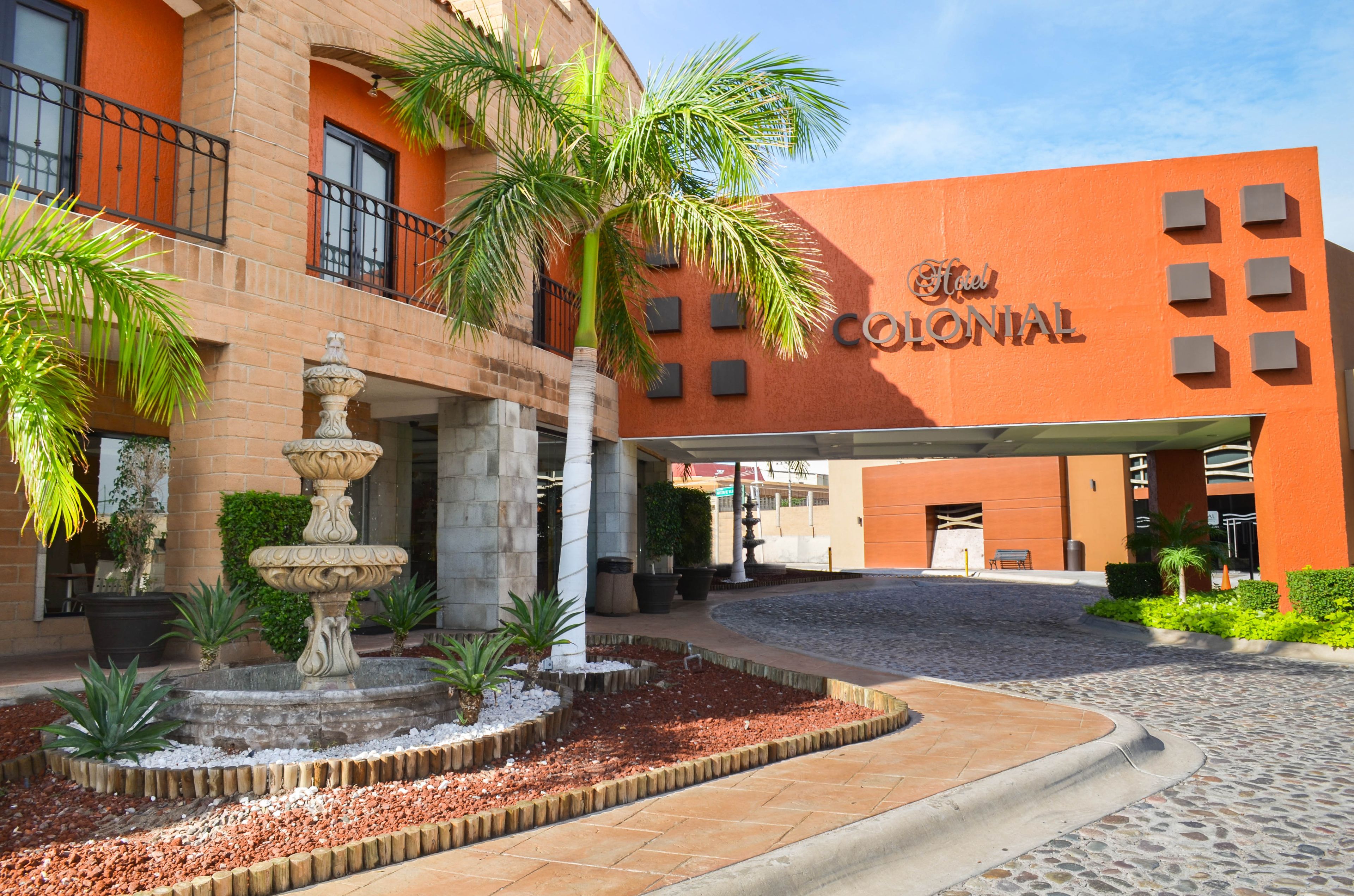 A hotel entrance with a fountain, palm trees, and a cobblestone pathway.