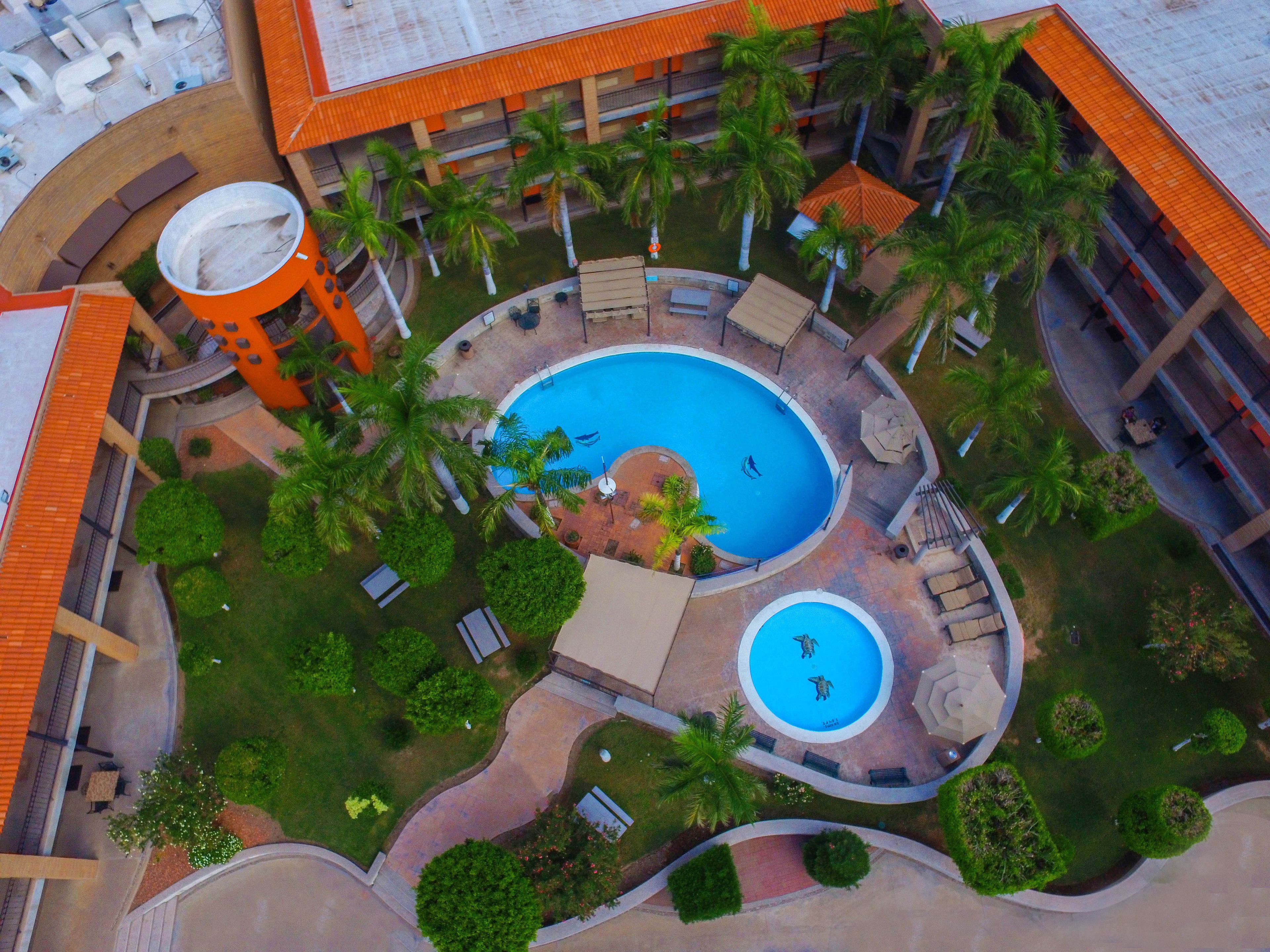 Vista aérea de un hotel con piscina central, palmeras y zonas de estar al aire libre.