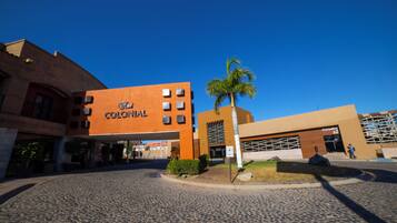 Un hotel llamado "Colonial" con diseño moderno, que presenta un patio empedrado y una palmera.