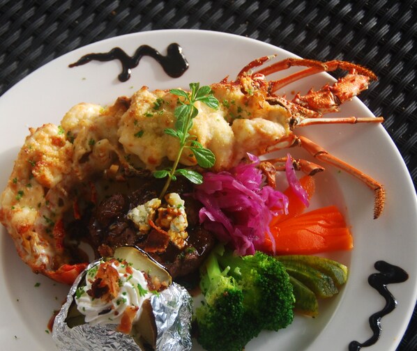 A plate of food with a lobster tail, vegetables, and a dollop of sauce.