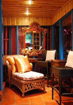 Une pièce avec un plafond en bois, un grand miroir décoratif, des meubles en osier et un sol carrelé.