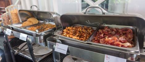 A buffet with labeled food options including fried breakfast potatoes and oven-baked bacon.