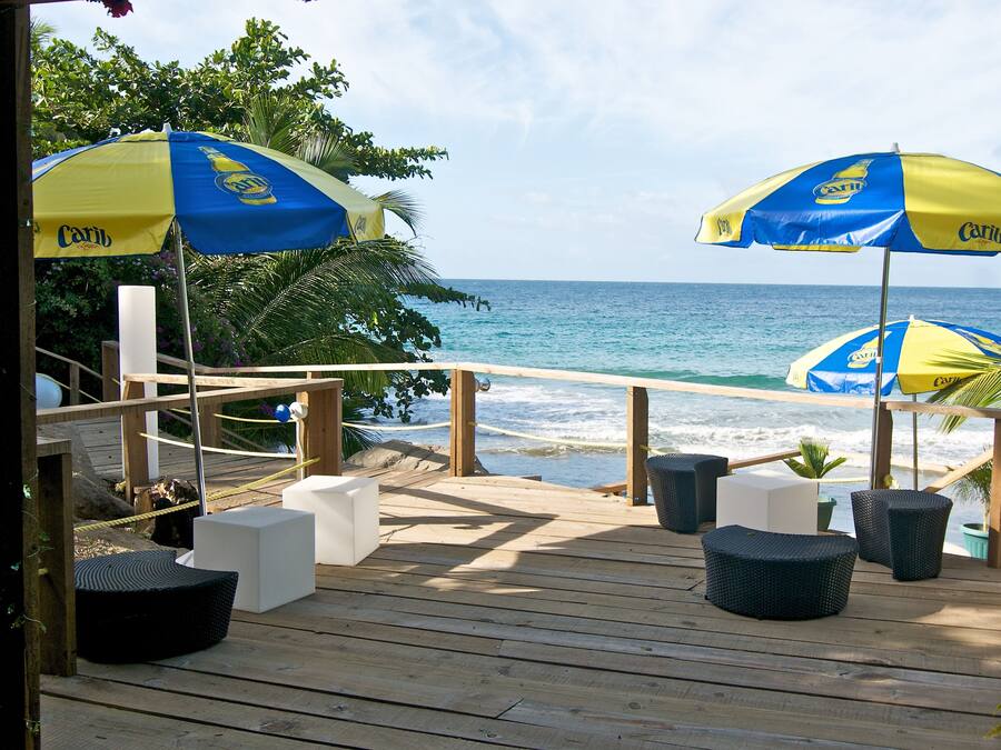 Een houten terras met buitenmeubels en parasols, met uitzicht op de oceaan.
