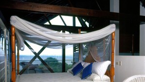 A bed with a canopy, a wicker chair, and a view of the outdoors. - Half Moon Blue (Scarborough)