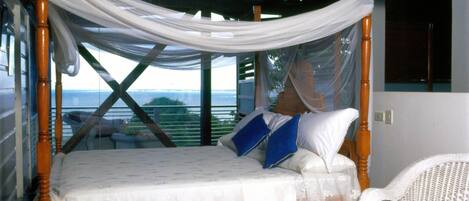 Una cama con dosel, una silla de mimbre y vistas al exterior.