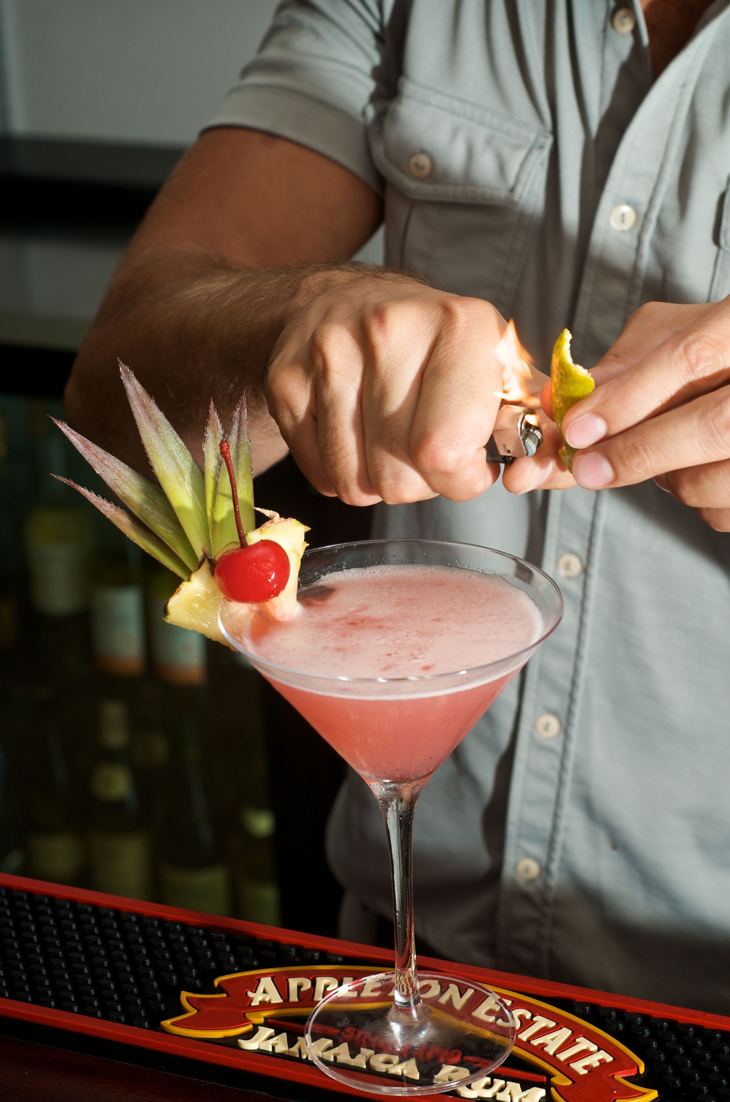 A bartender garnishing a pink cocktail with a pineapple slice and a cherry.