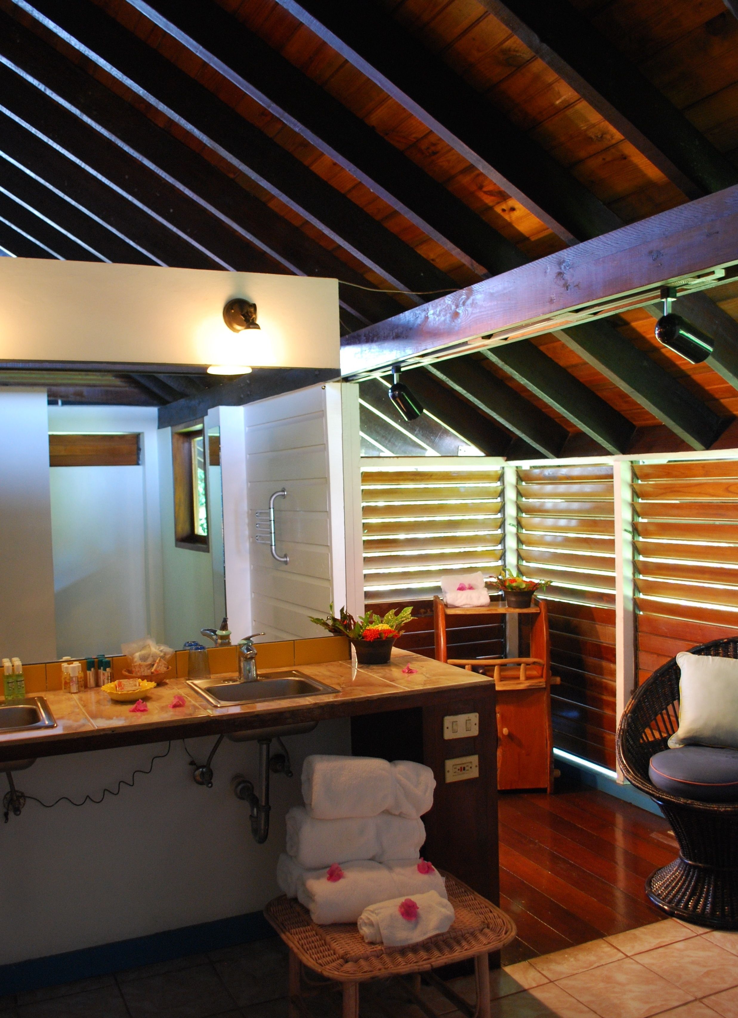 A kitchen with a sink, a countertop, and a mirror. There are towels stacked on a chair and a potted plant on the counter.