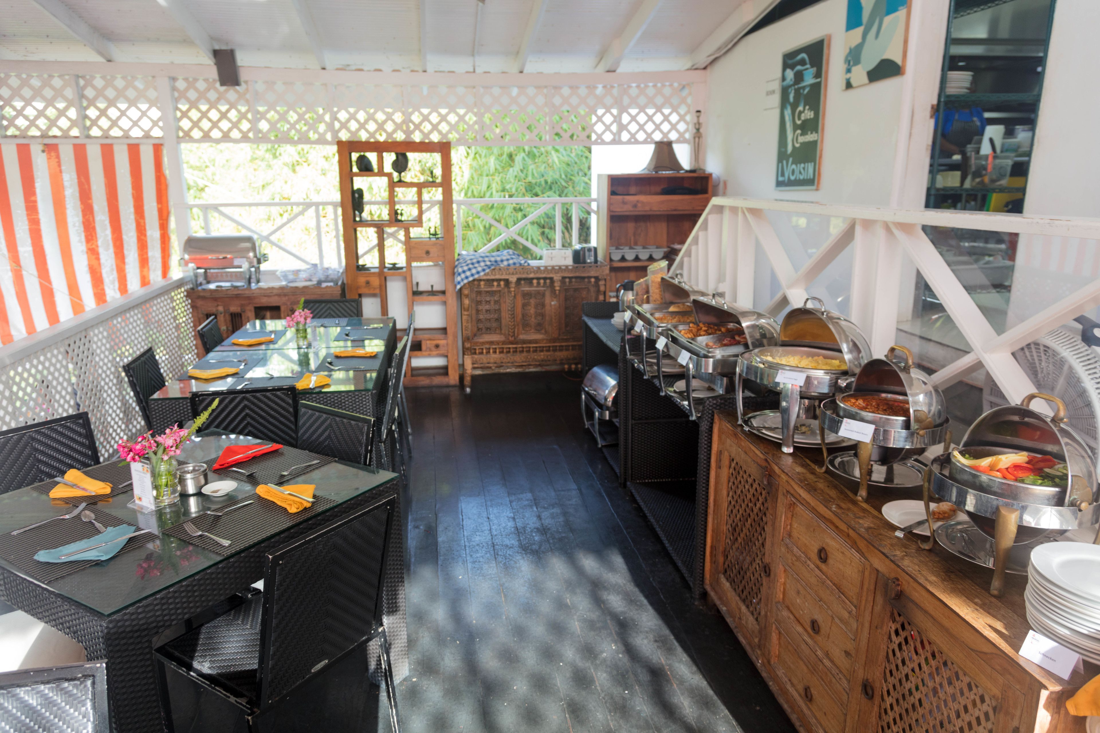 A buffet setup with multiple serving stations, a dining area with tables and chairs, and a wooden counter with various food containers.
