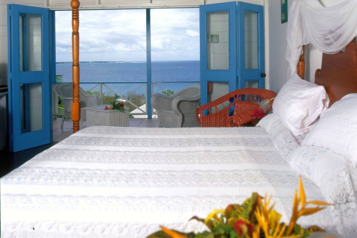 Un dormitorio con cama, vista al mar y balcón con sillas.