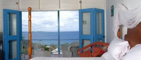 Quarto com cama, vista para o mar e varanda com cadeiras.