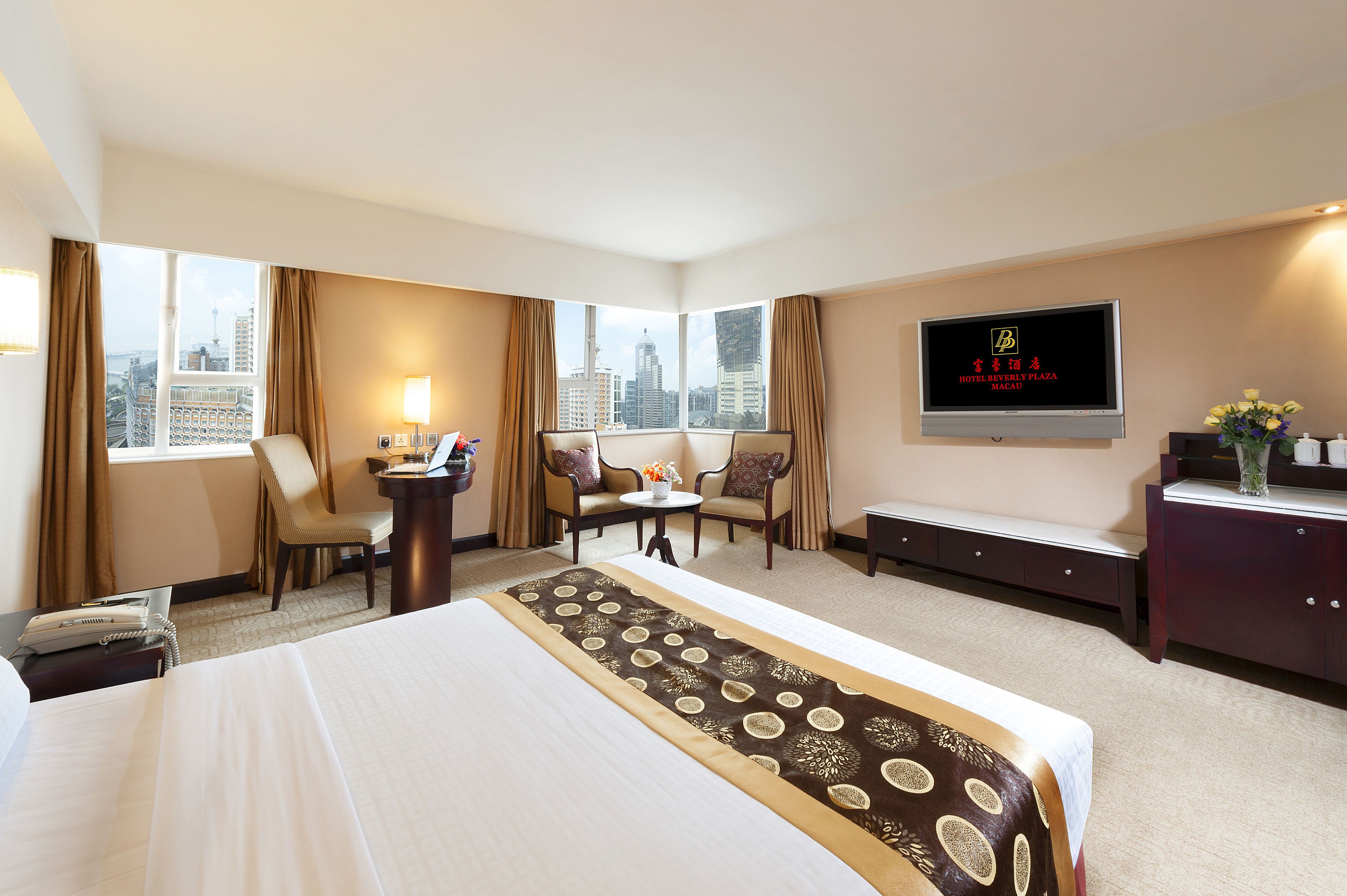 A hotel room with a large bed, two armchairs, a small table, a desk, a TV, and a city view.