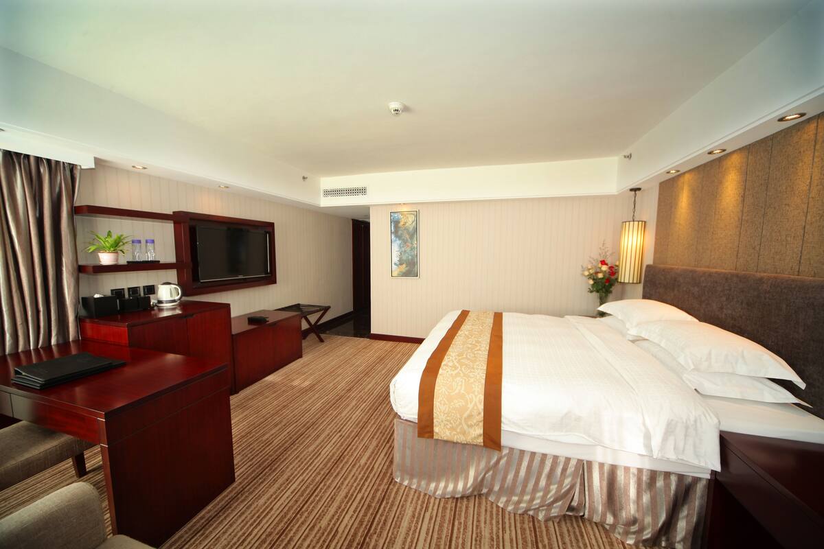 Habitación de hotel con cama, escritorio, silla, televisor y un cuadro en la pared.
