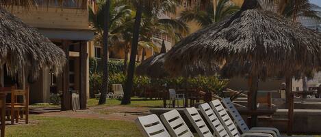 A beachside lounge area with wooden tables and lounge chairs under thatched umbrellas.