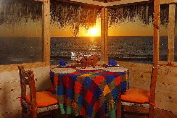 A wooden dining area with a table set for two, overlooking the ocean at sunset. - Villas El Rancho (Mazatlán)